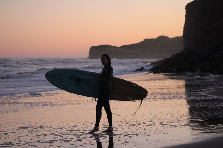 Surfista con su tabla al atardecer junto al acantilado